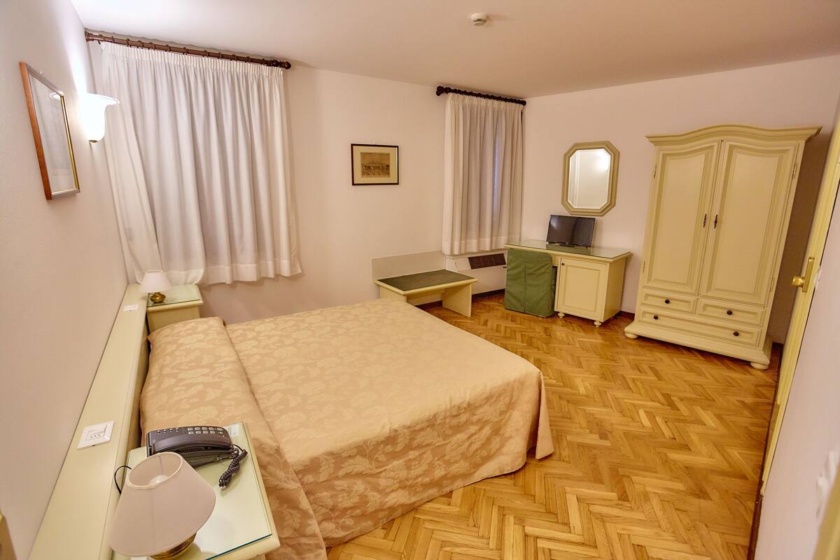 A hotel room with a bed, bedside table, lamp, telephone, and wardrobe.