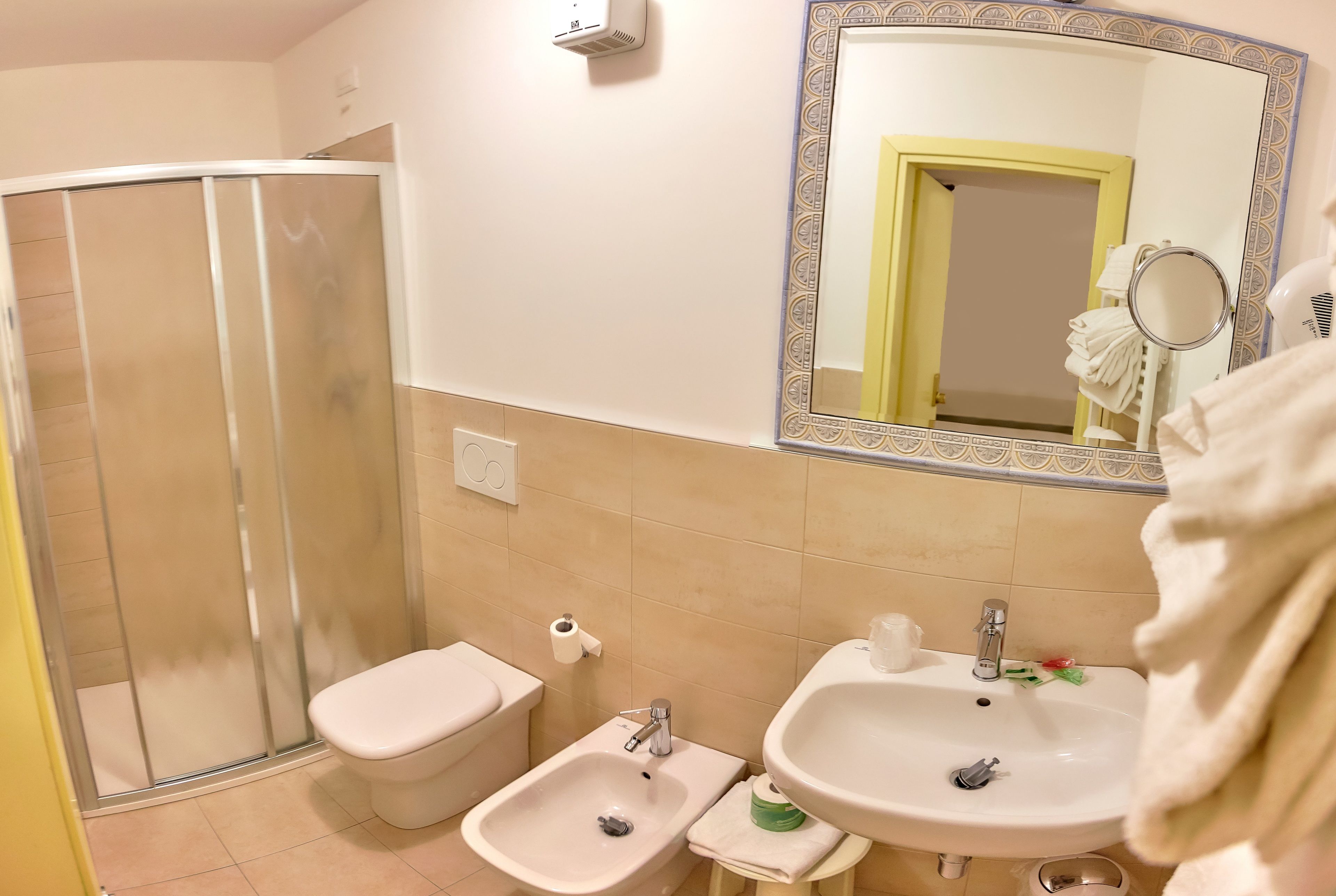 Een badkamer met een douche, toilet, bidet, wastafel en een spiegel.