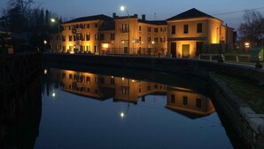 Un immeuble situé au bord de l’eau, avec plusieurs étages, un canal devant et des lampadaires dans la rue.