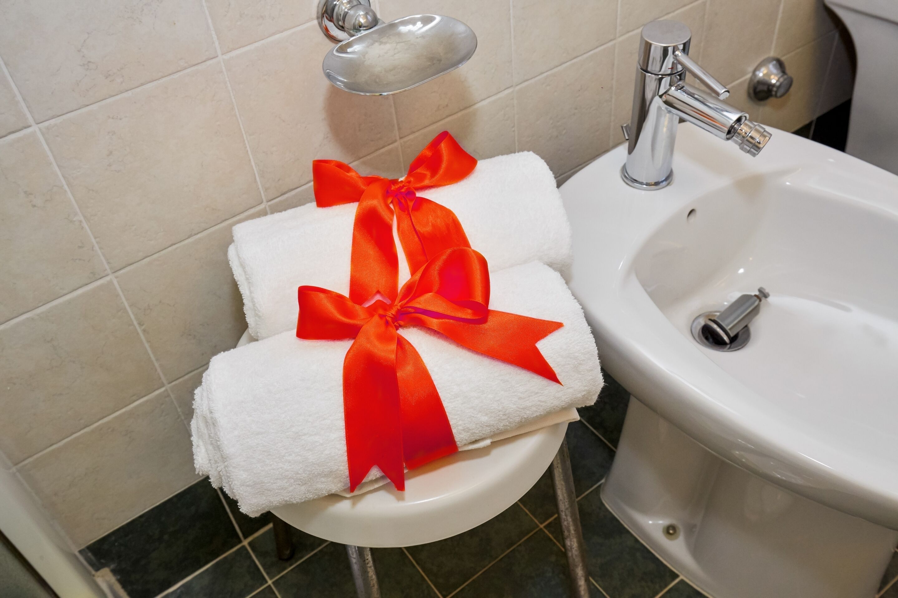 A bathroom with a white sink, a toilet, and a towel rack with two white towels tied with an orange ribbon.