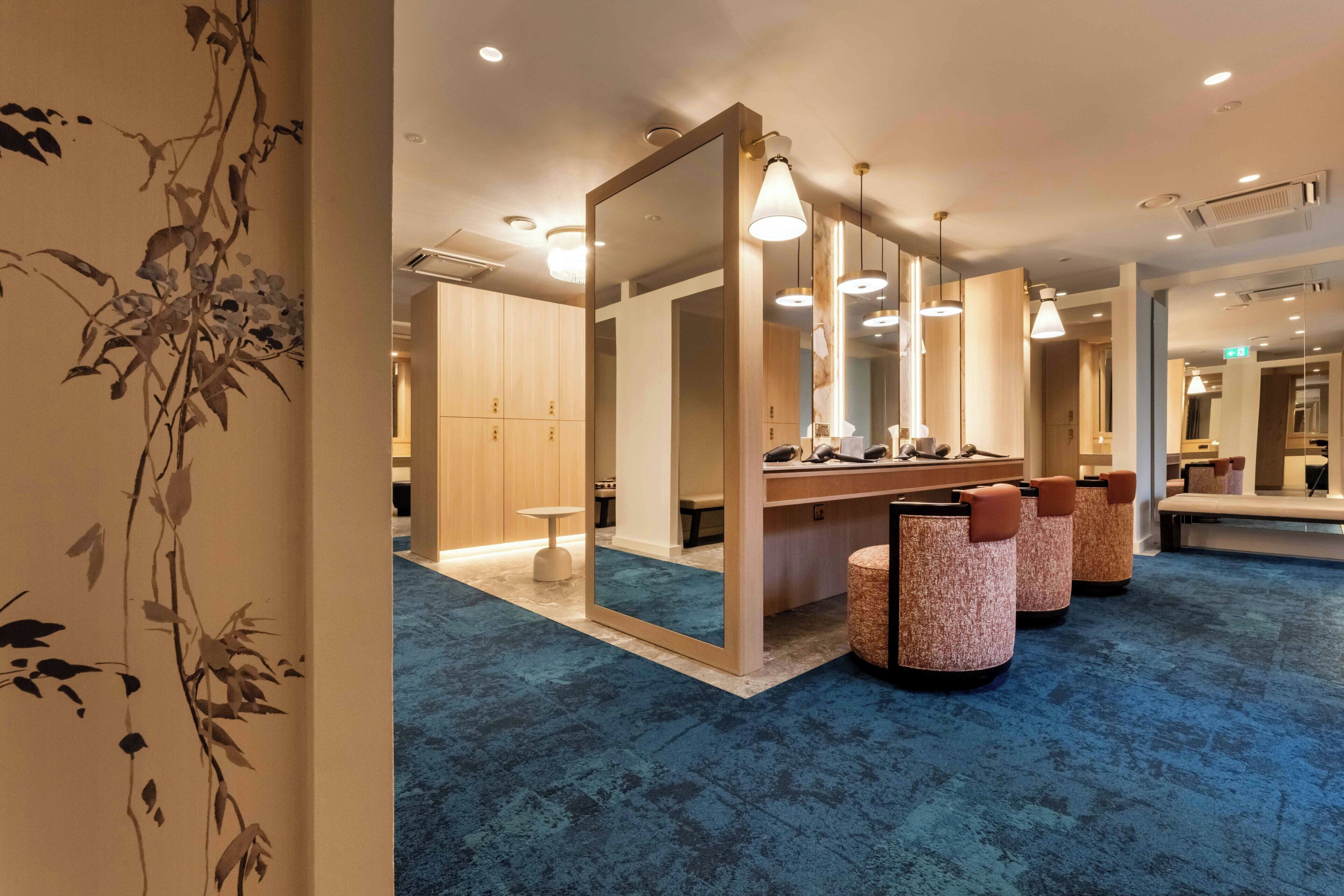 A hotel room with a large mirror, a vanity with a sink, and a seating area with cushioned chairs.