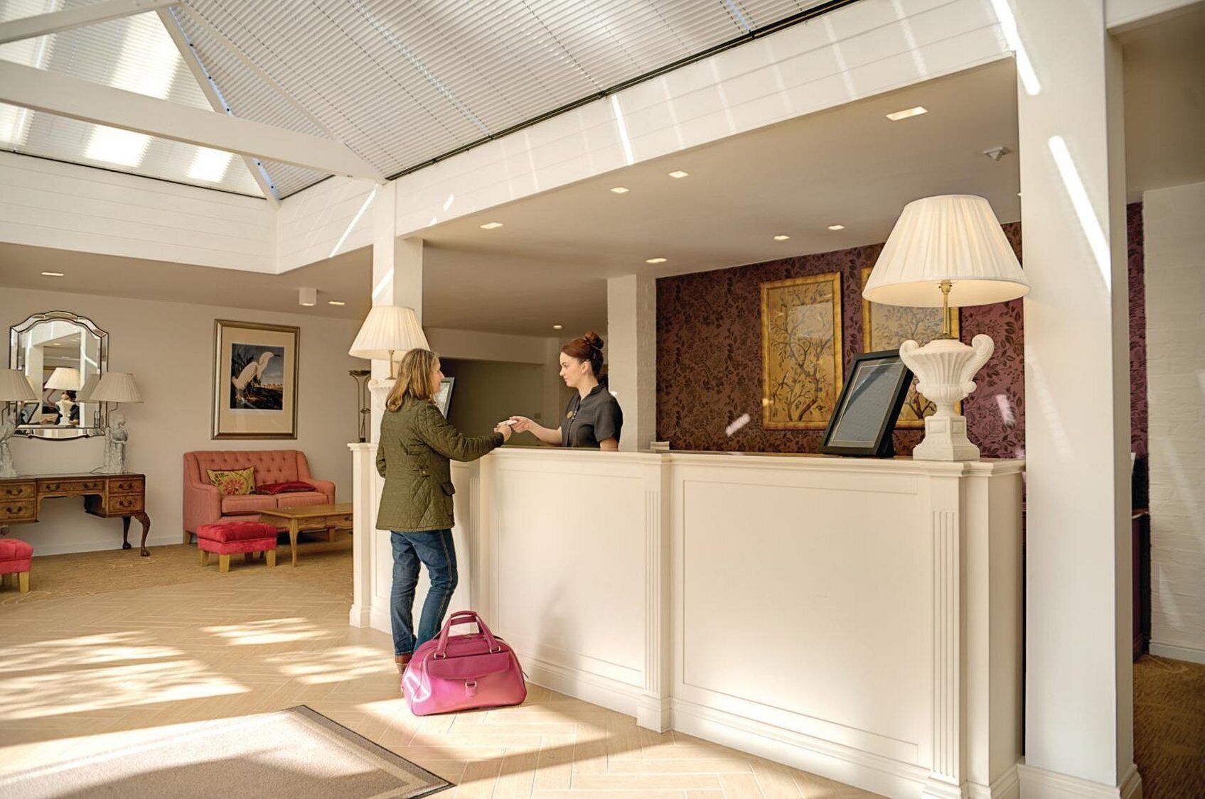 A reception area with a reception desk, a pink sofa, a wooden cabinet, and a framed picture on the wall.