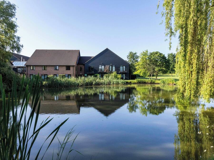 Een rustige woonwijk met een huis aan een kalm meer, omgeven door weelderige begroeiing en bomen.