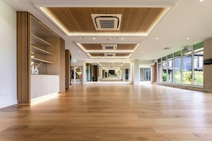 Un pasillo amplio con suelo de madera, iluminación empotrada y grandes ventanales a un lado.