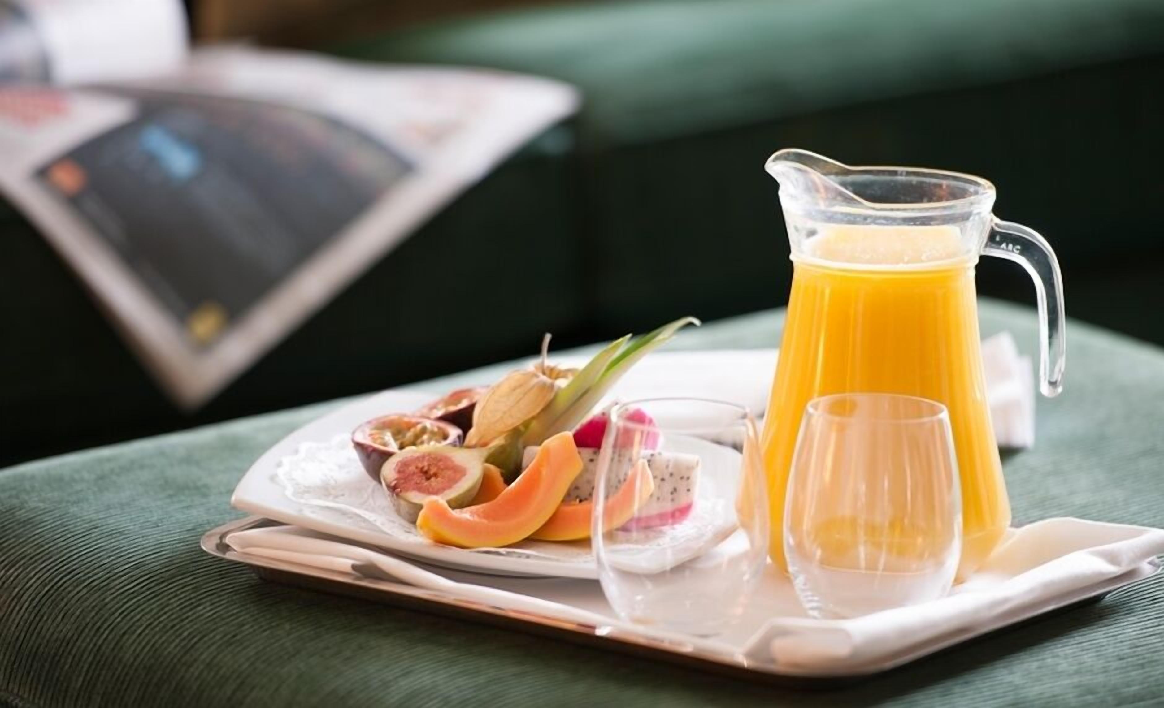 A breakfast tray with a pitcher of orange juice, a glass, and a plate with sliced fruits and a small bowl of yogurt.