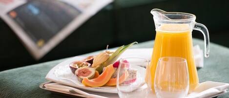 Bandeja de desayuno con un jarro de jugo de naranja, un vaso, y un plato de frutas cortadas con un tazón pequeño de yogur.