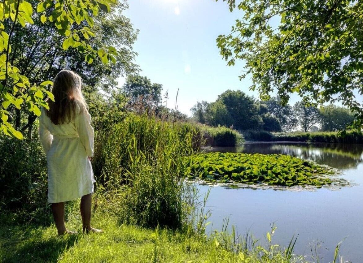 A person standing by a calm lake surrounded by lush greenery and trees.