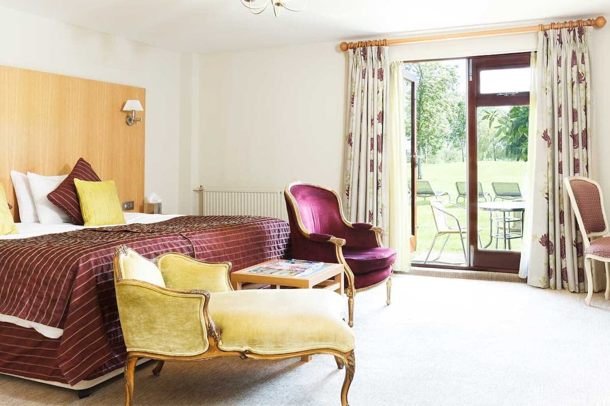 A hotel room with a large bed, two chairs, a desk, and a television.