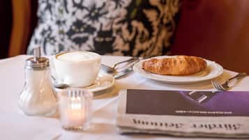 Une table avec un croissant, une tasse de café, une bougie et un journal.