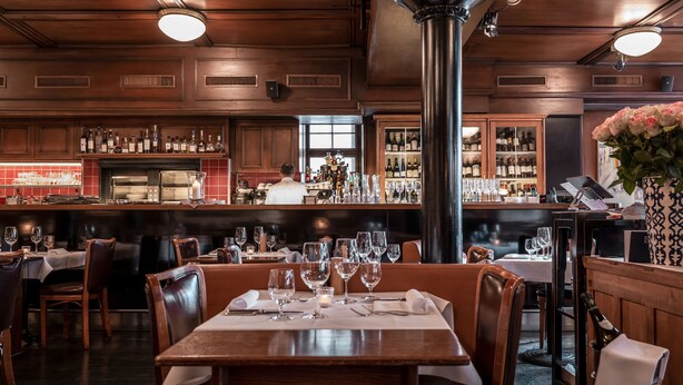 Un restaurant au décor en bois, avec un espace bar et des tables dressées pour le service.