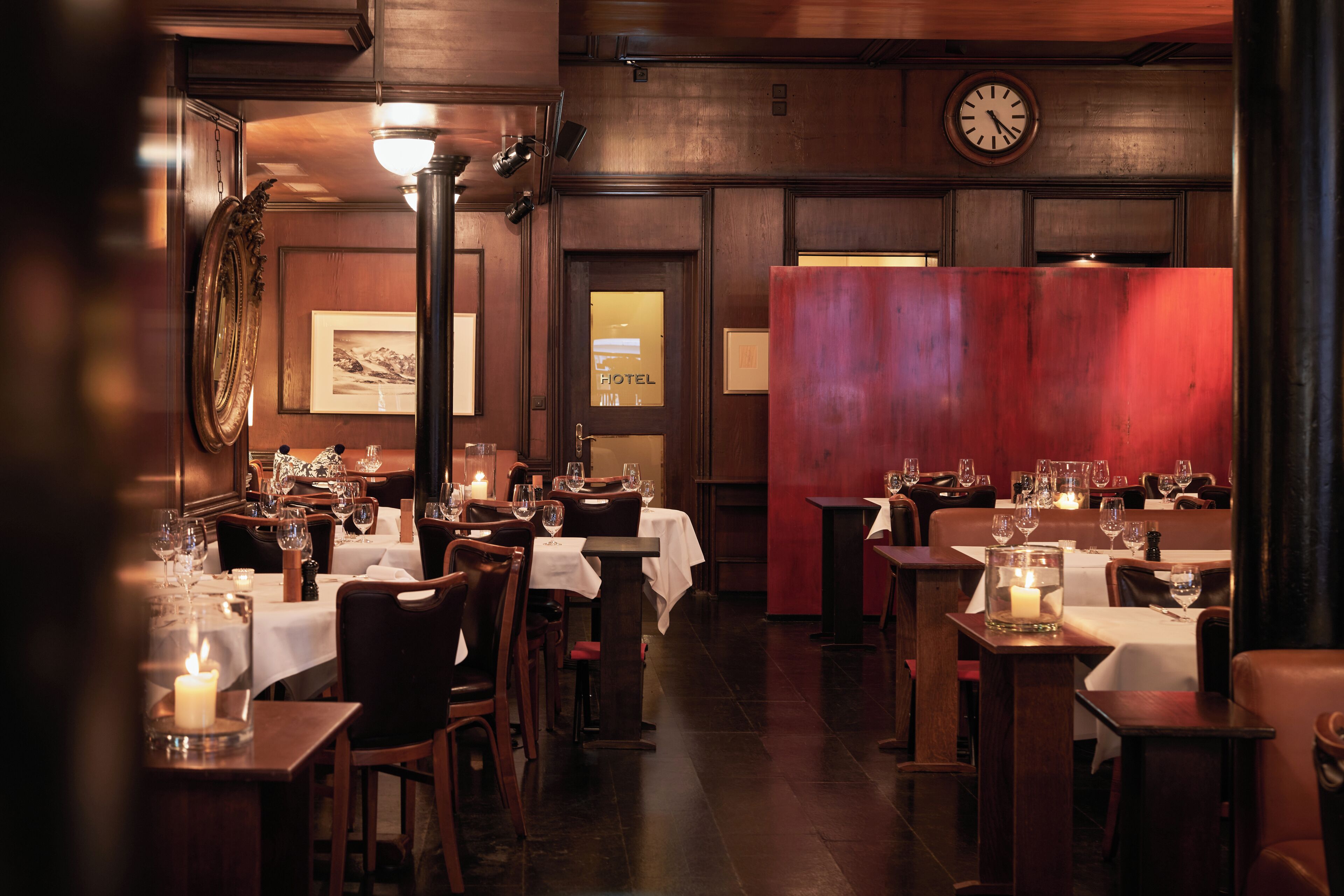 A restaurant with wooden walls, tables with white tablecloths, and candles on the tables.