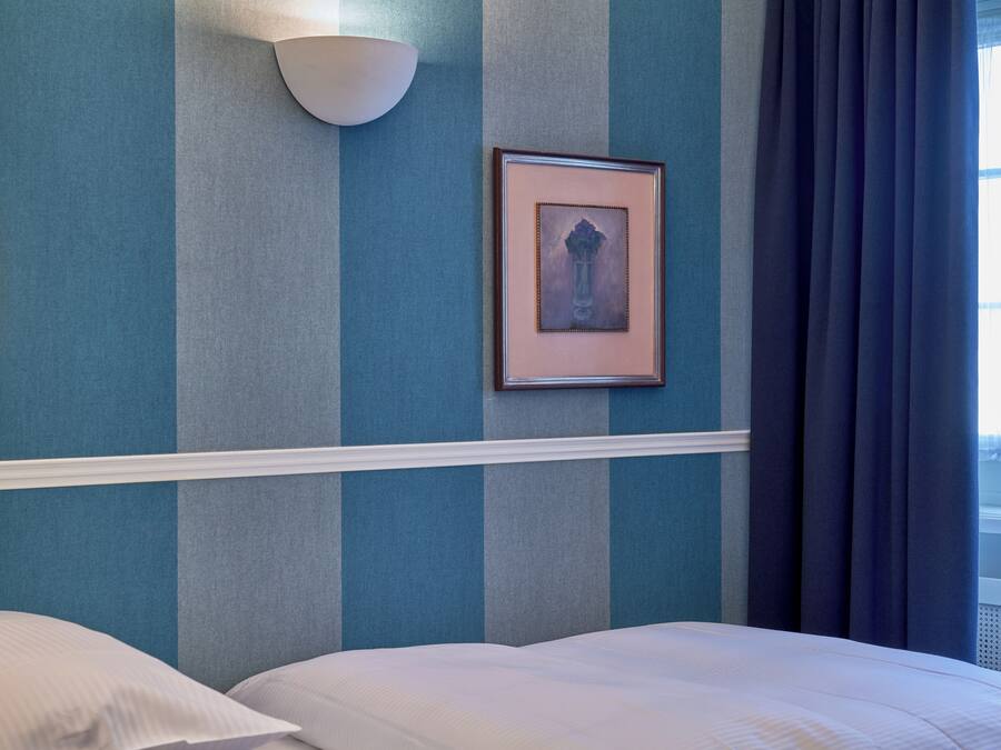 Una habitación de hotel con una cama, una lámpara de pared y un cuadro enmarcado.