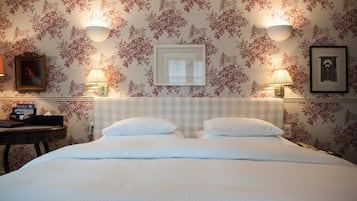 A neatly made bed with a checkered headboard, two bedside lamps, and floral wallpaper.