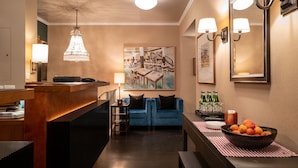 Un hall d’hôtel moderne avec un comptoir d’accueil, un canapé bleu, un lustre et un tableau représentant une bibliothèque.