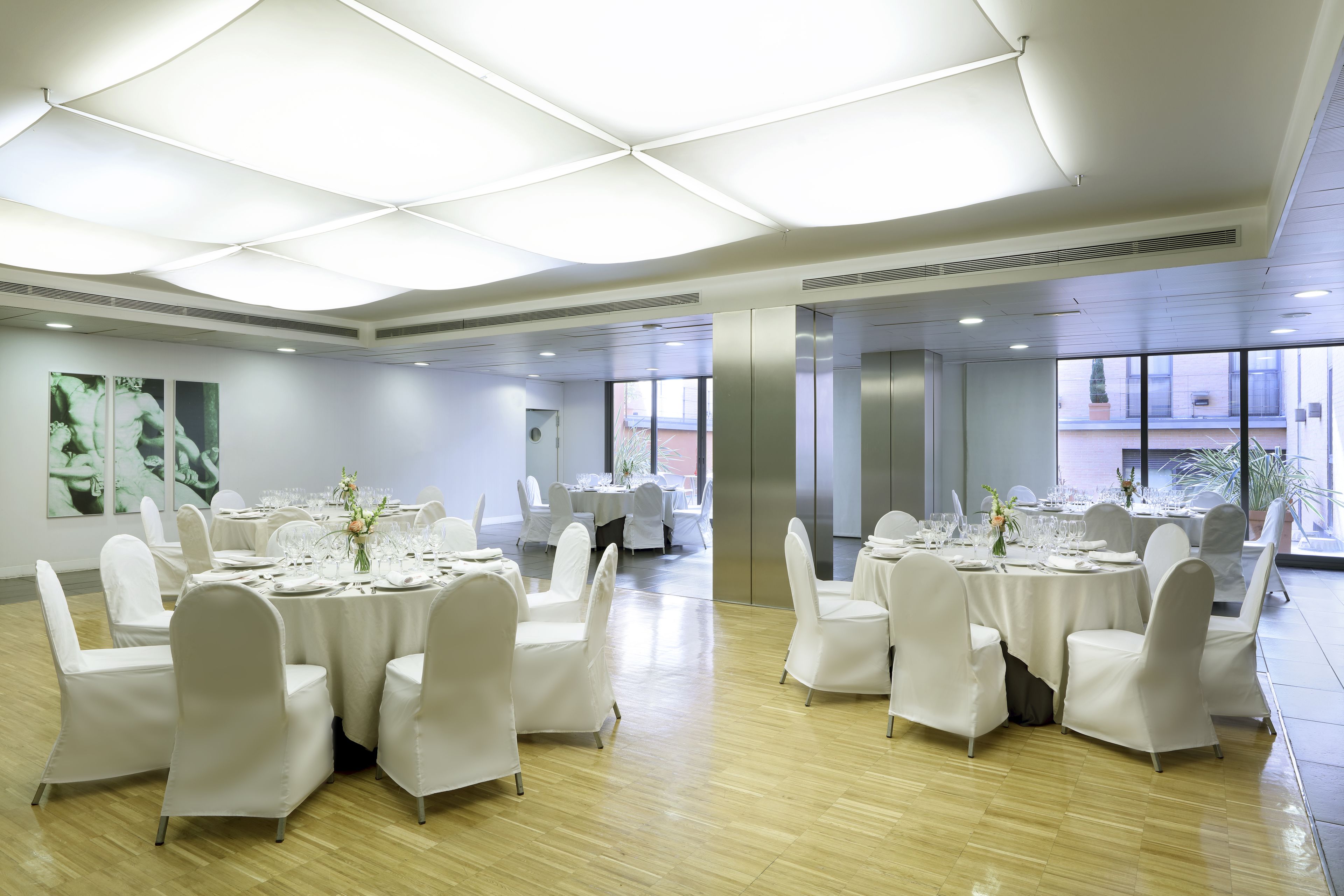 A spacious banquet hall with round tables set for dining, white chairs, and a modern ceiling design.