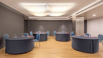Un salón de conferencias con cuatro mesas redondas, cada una con sillas y botellas de agua.