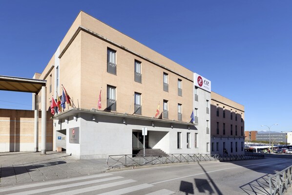 Un edificio con un letrero que dice 'Exc Hotels'. Tiene techo plano, varias ventanas y una escalera que lleva a la entrada.