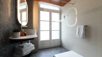 Un baño moderno con tocador, un espejo grande, lavamanos, toallero y zona de ducha.
