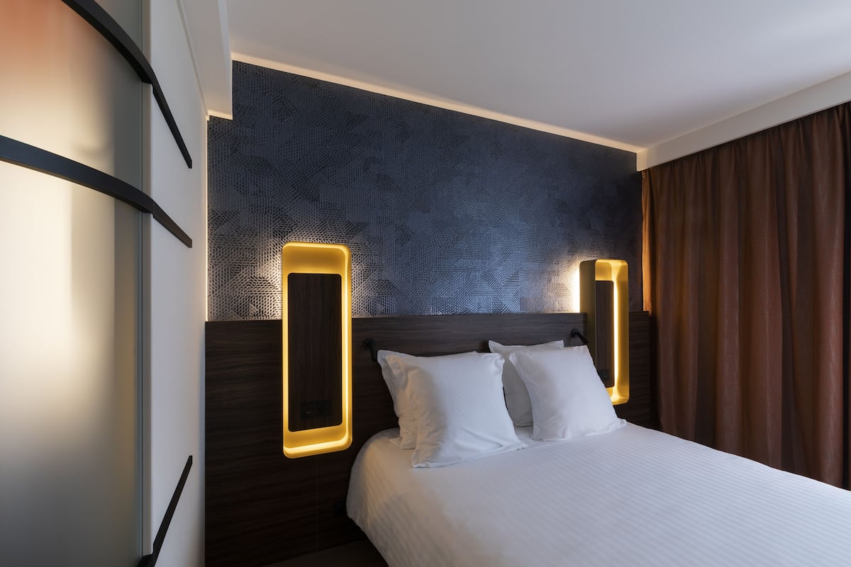 Una camera d'albergo moderna con un letto grande, una testiera in legno scuro e due lampade a parete.