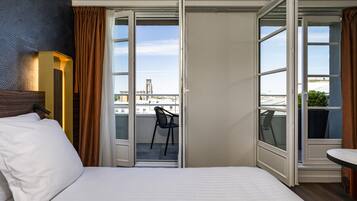 Una habitación de hotel con cama, una silla y un balcón con vistas a la ciudad.