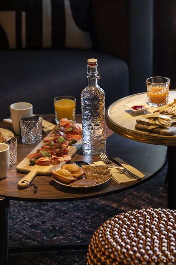 A breakfast setting with a wooden board, a bottle, and a glass of orange juice on a round table.