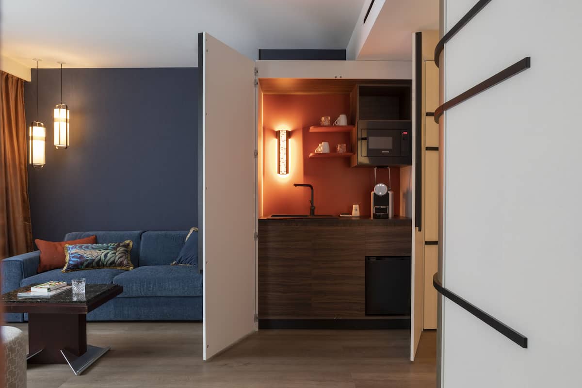 Un soggiorno moderno con un divano blu, un tavolino da caffè e un angolo cucina con forno a microonde e scaffali.