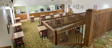 A spacious interior with a high ceiling, a staircase with a floral carpet, and a dining area with wooden tables and chairs.