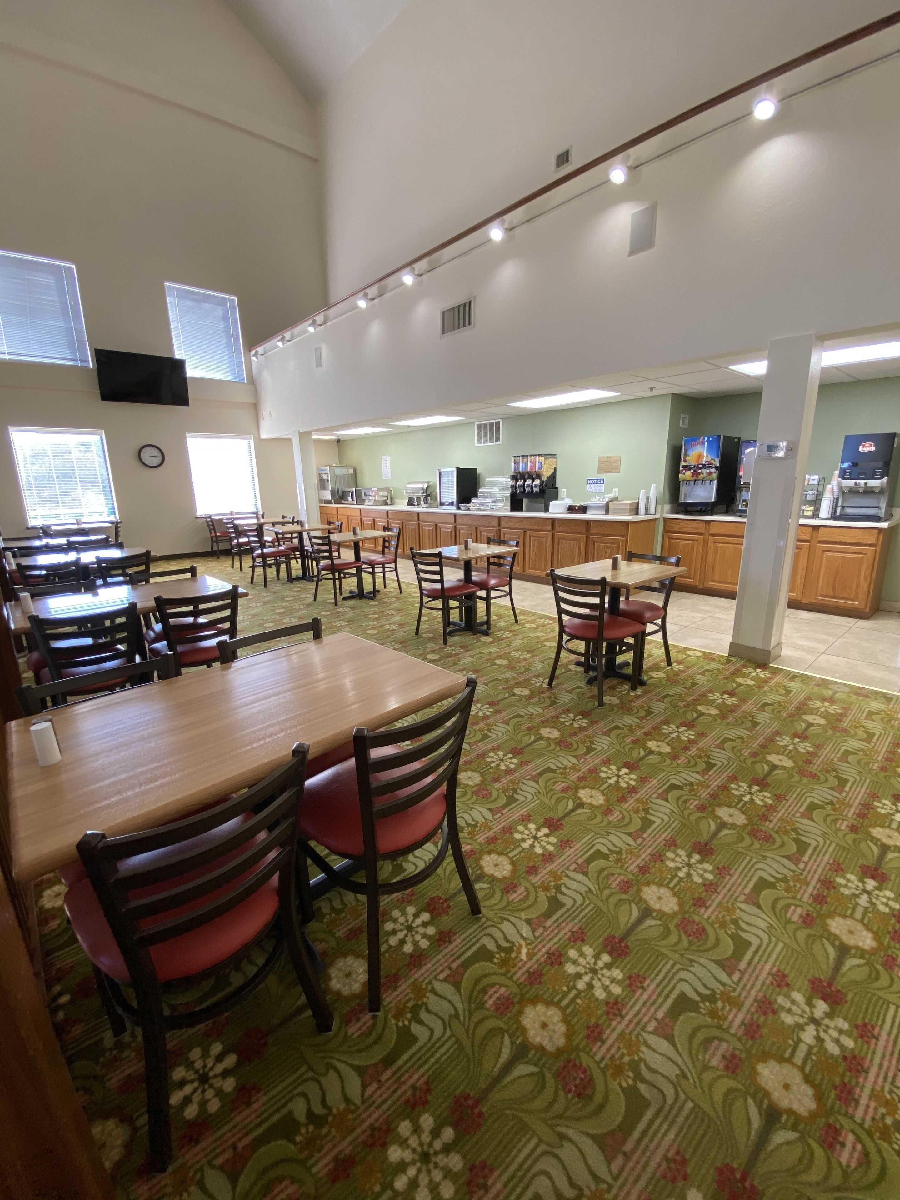 A spacious dining area with multiple tables and chairs, a coffee station, and a kitchen area in the background.