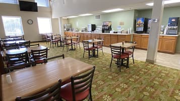 Un grand espace de restauration avec plusieurs tables et chaises, un coin café et une cuisine en arrière-plan.