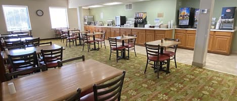 A spacious dining area with multiple tables and chairs, a coffee station, and a kitchen area in the background.