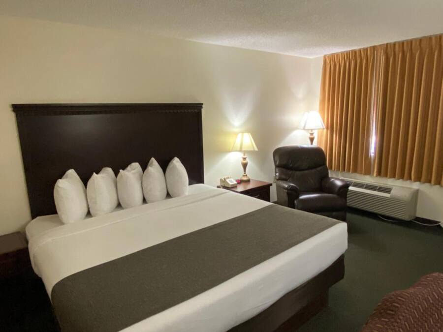 A hotel room with a large bed, a desk, a chair, and a window with curtains.