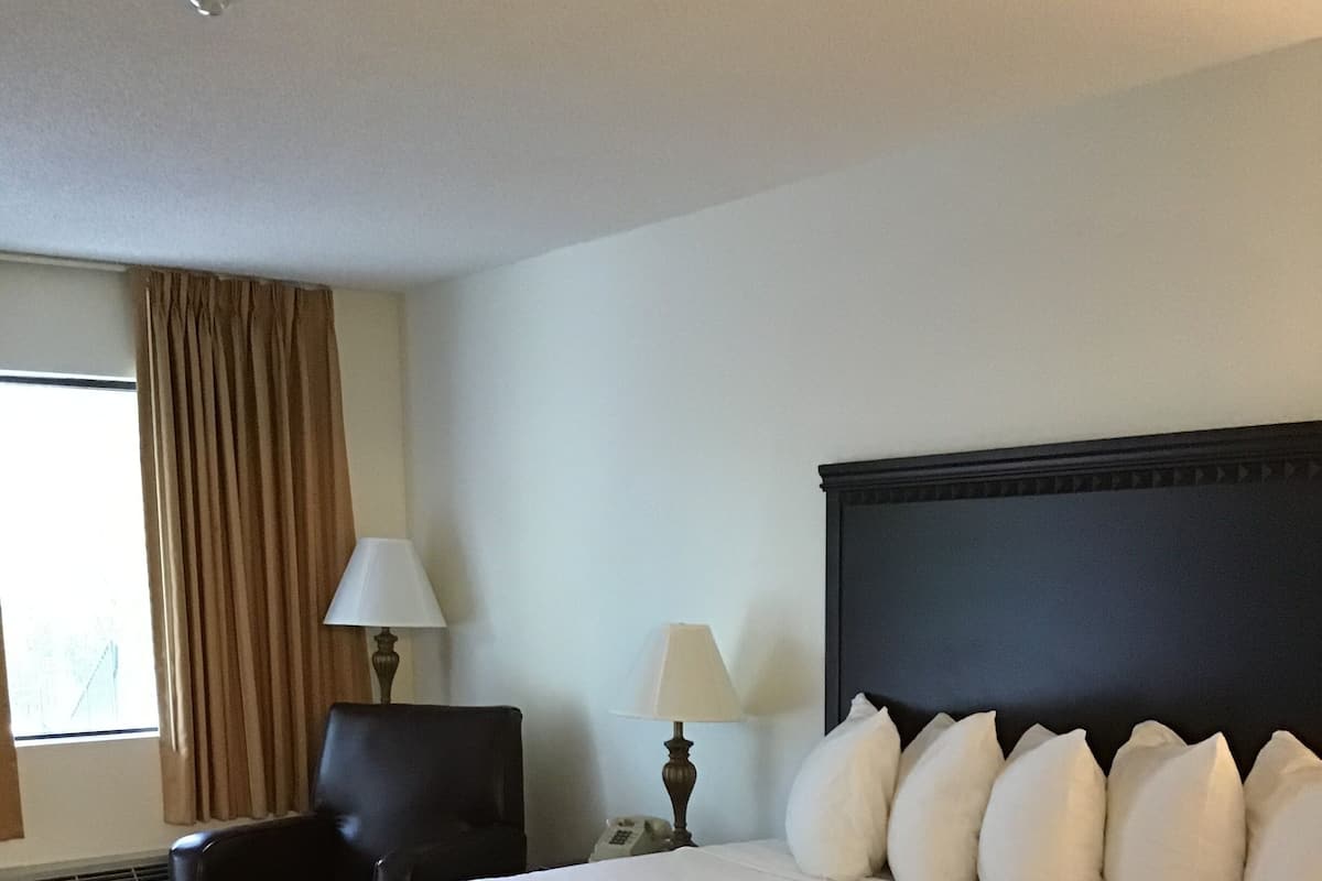 Una habitación de hotel con una cama grande, dos lámparas de noche, una silla y un ventanal con cortinas.
