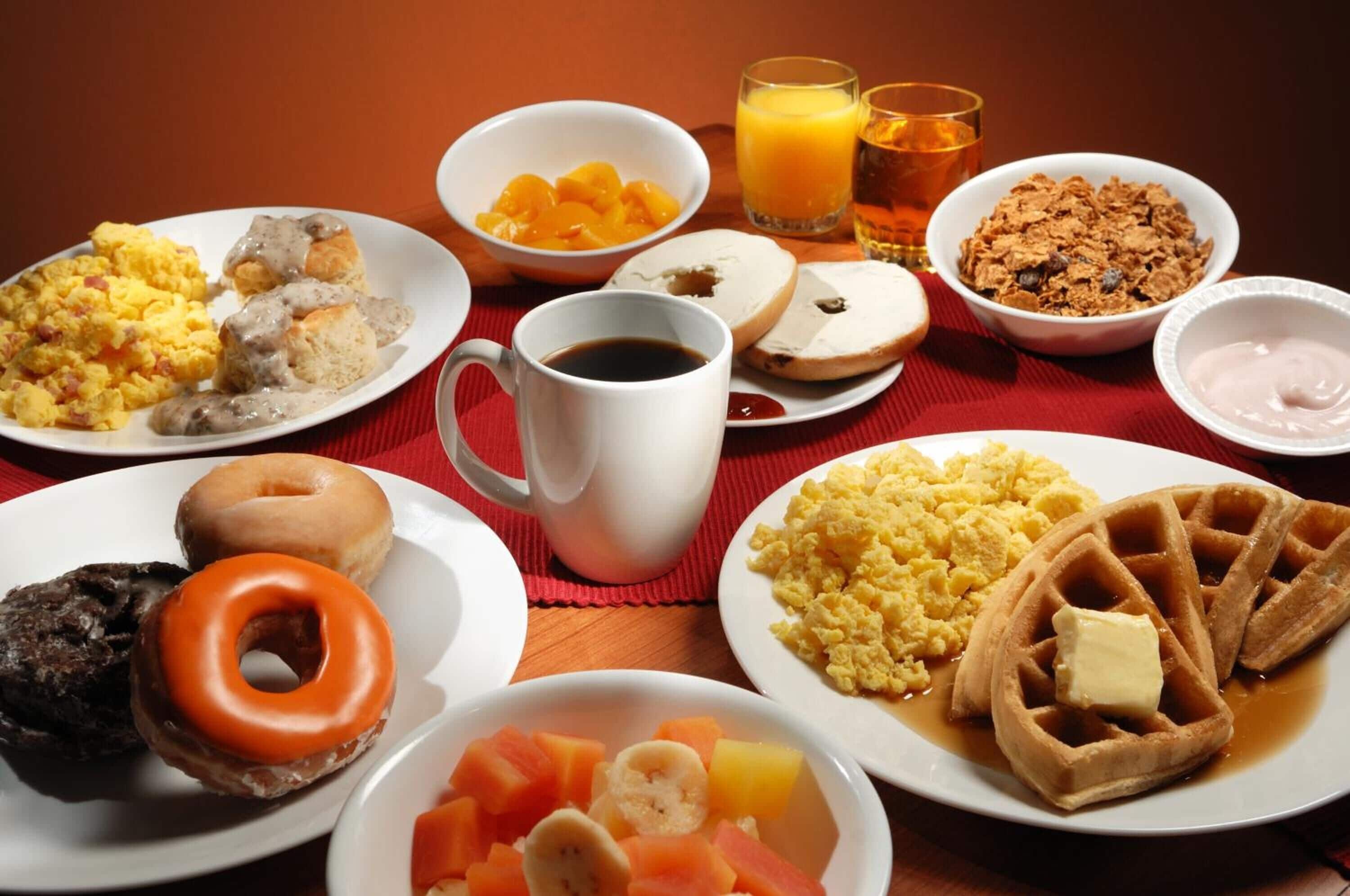 Una mesa de desayuno con diferentes platos, incluyendo huevos revueltos, gofres y pasteles.