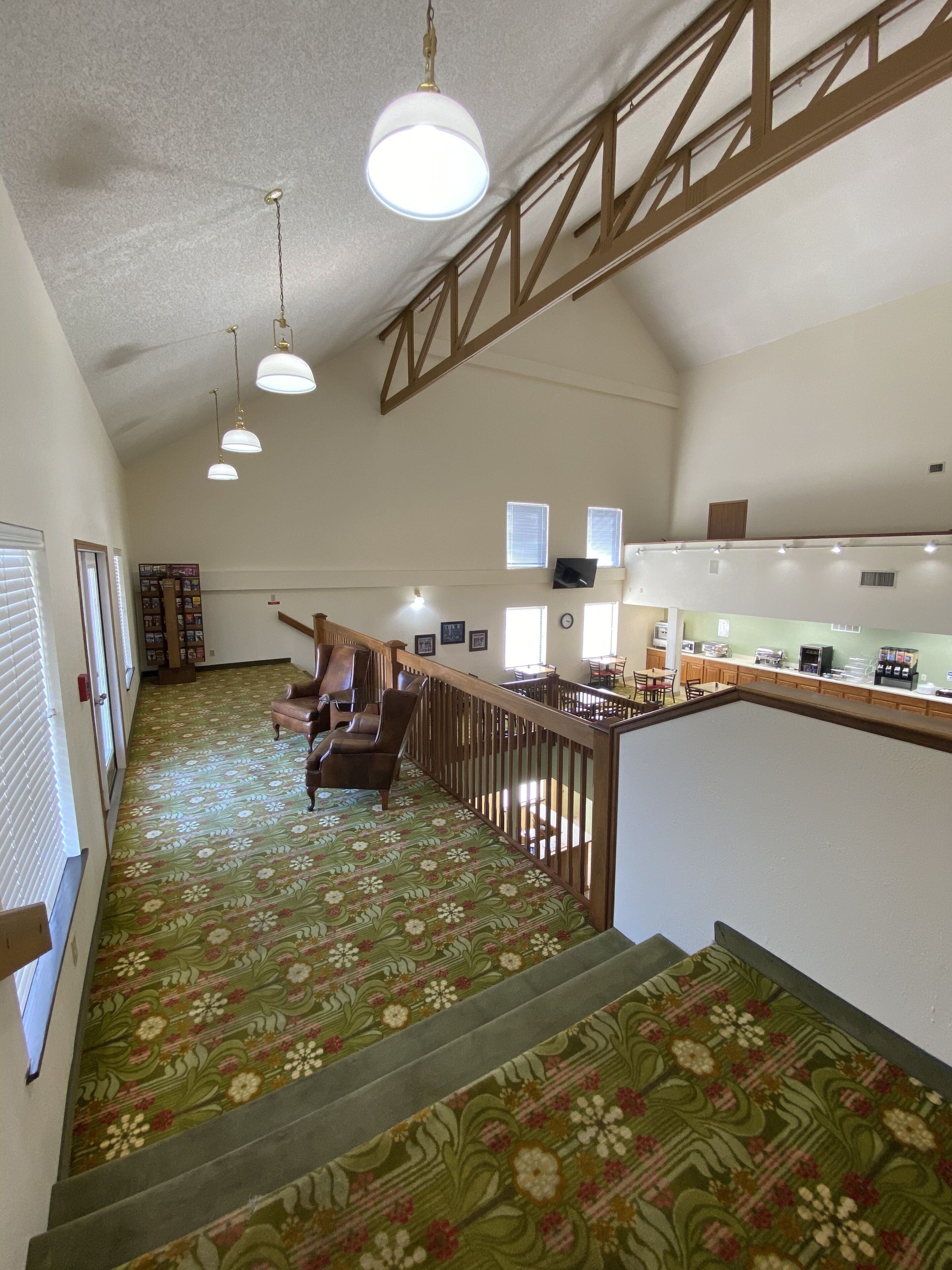 A spacious hallway with a wooden staircase, a seating area with chairs, and a kitchenette area with a counter and appliances.