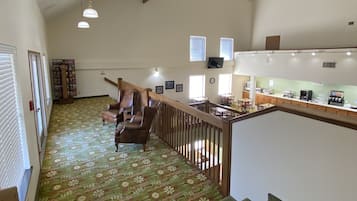 A spacious hallway with a wooden staircase, a seating area with chairs, and a kitchenette area with a counter and appliances.