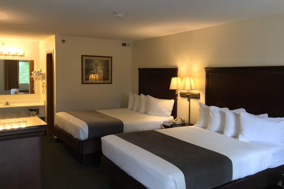 Habitación de hotel con dos camas, un escritorio, un espejo y un cuadro en la pared.