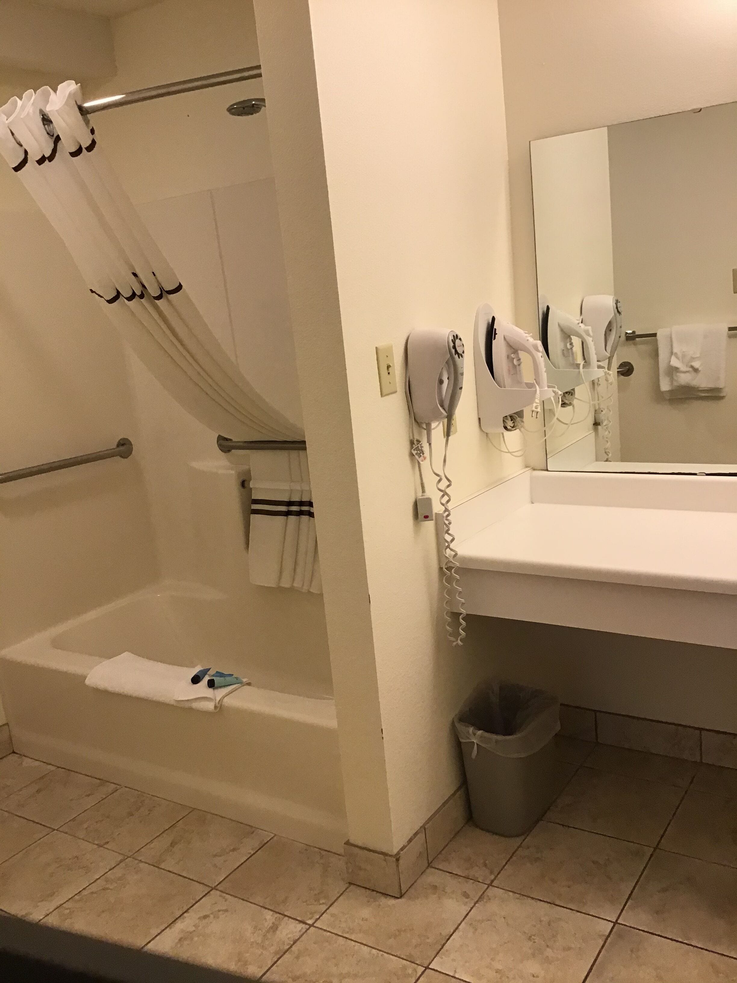 A bathroom with a bathtub, a shower curtain, a towel rack, a hairdryer, and a trash can.