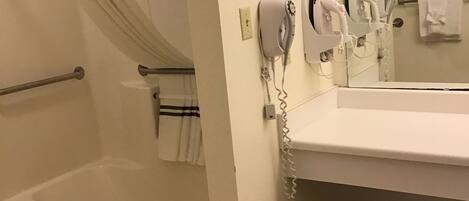 A bathroom with a bathtub, a shower curtain, a towel rack, a hairdryer, and a trash can.