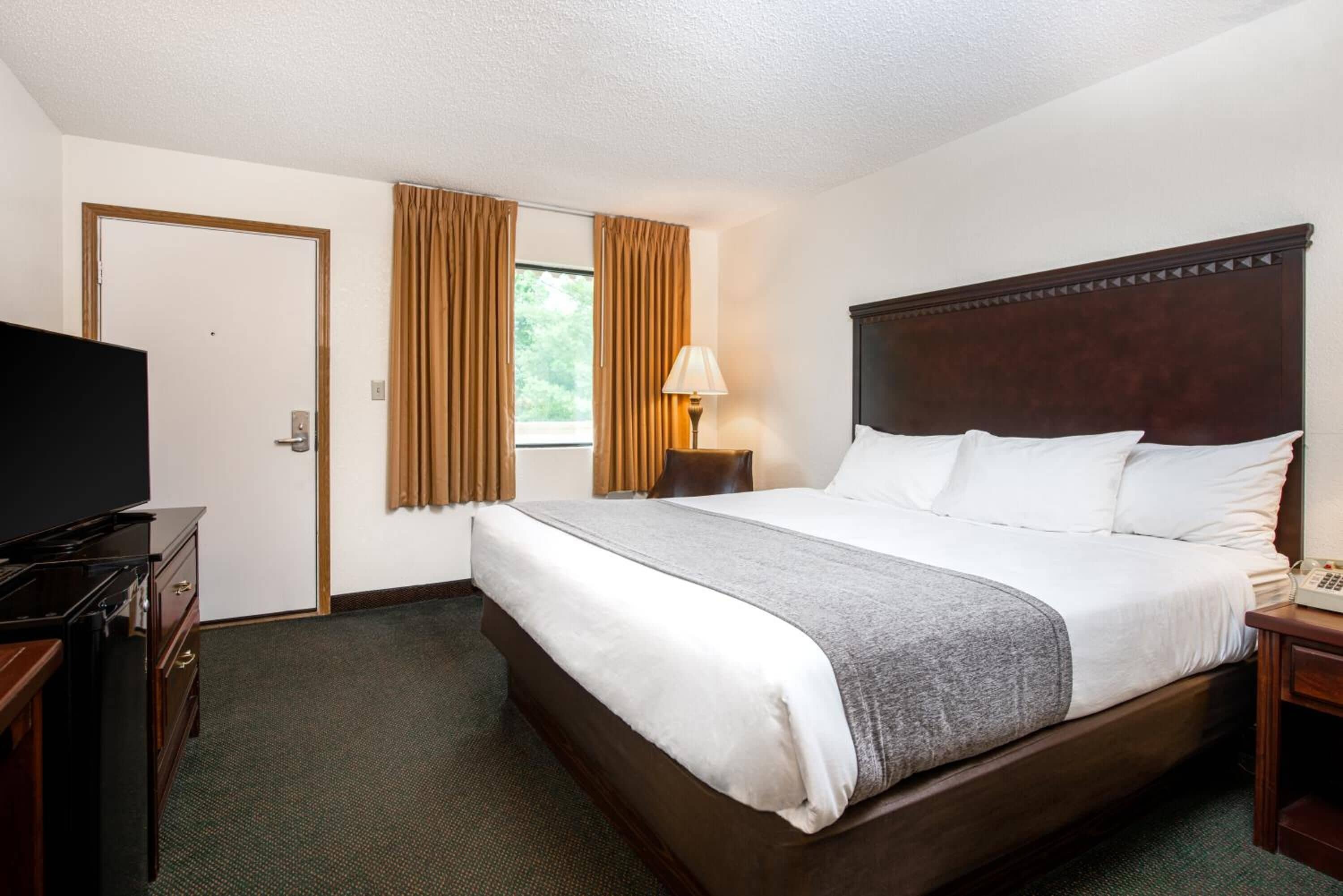 Una habitación de hotel con una cama grande, televisión, escritorio y ventana con cortinas.