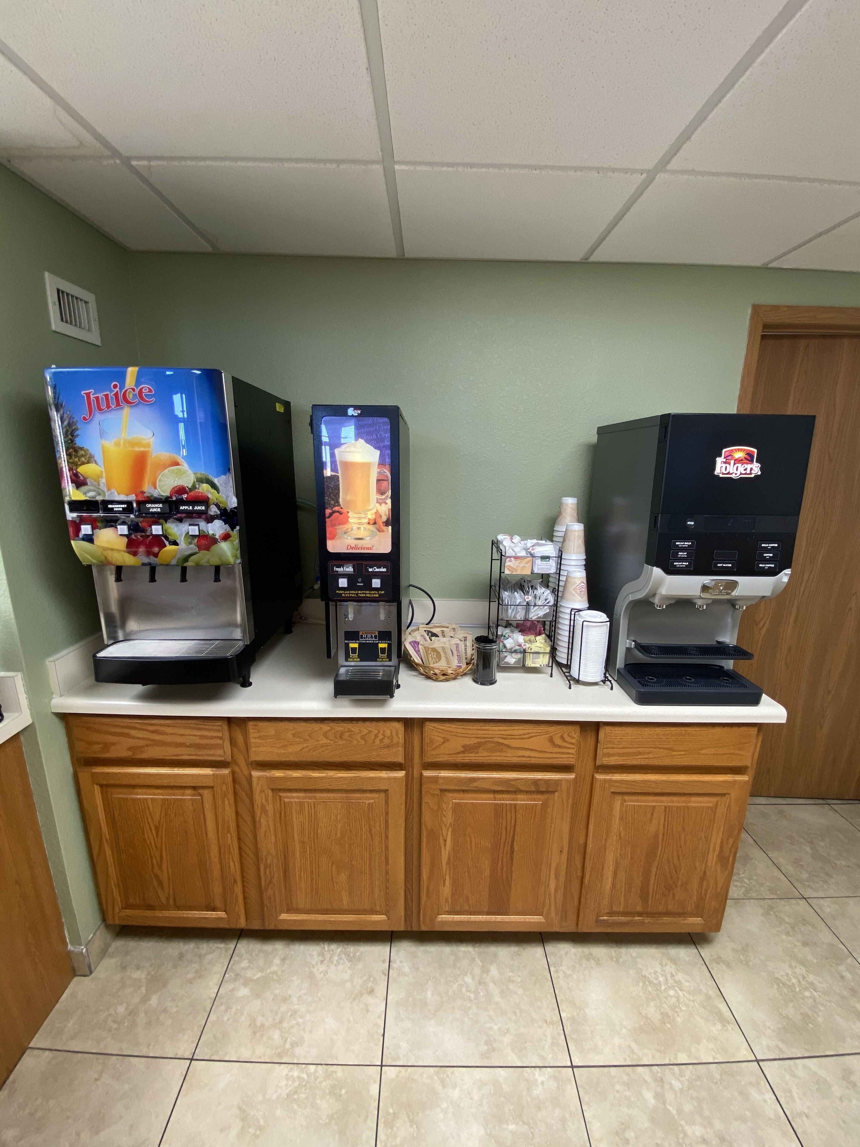 A self-service beverage station with multiple drink dispensers, including juice and coffee options, and a cash register.