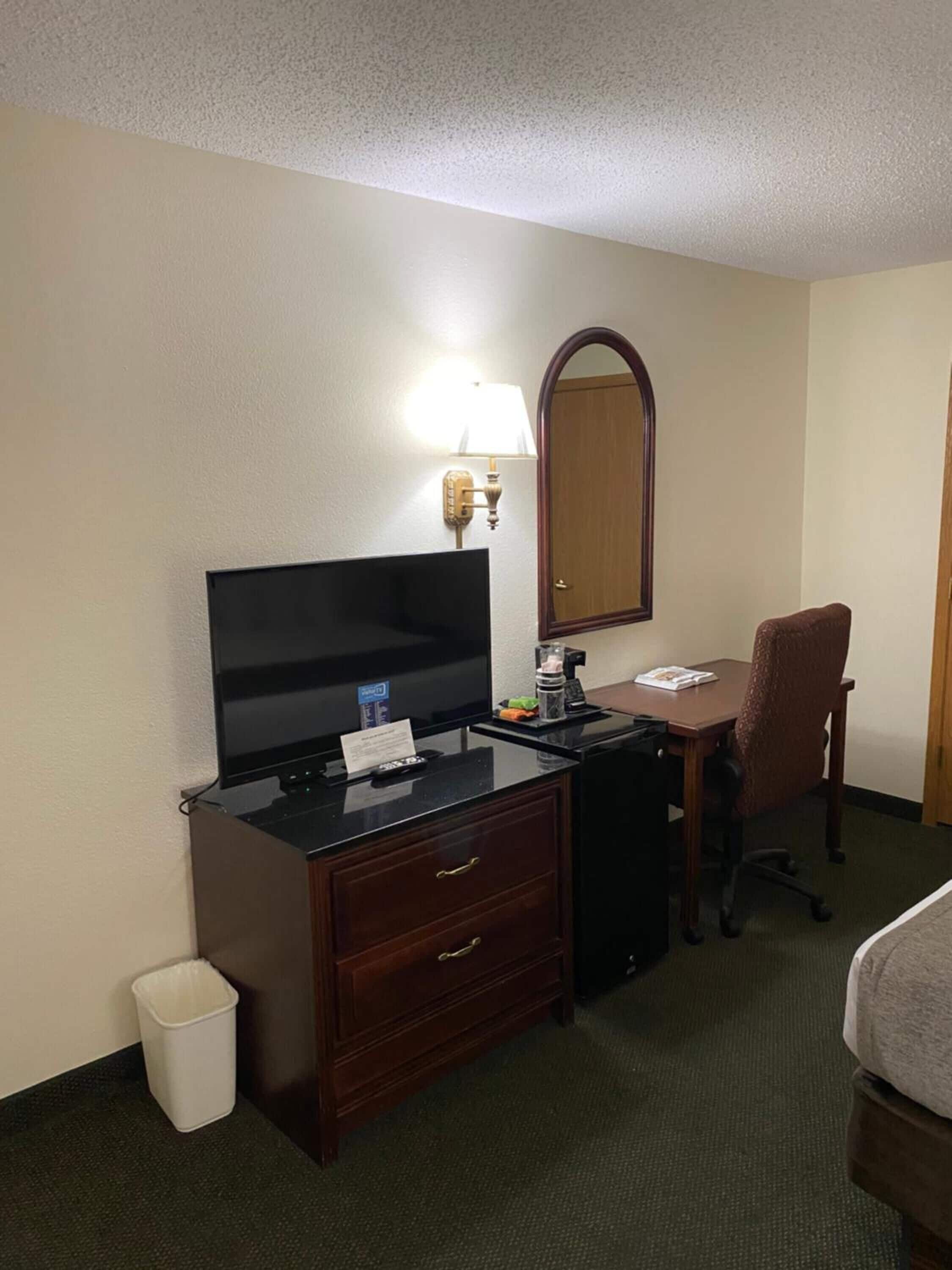 Una habitación de hotel con escritorio, silla, televisor y espejo.