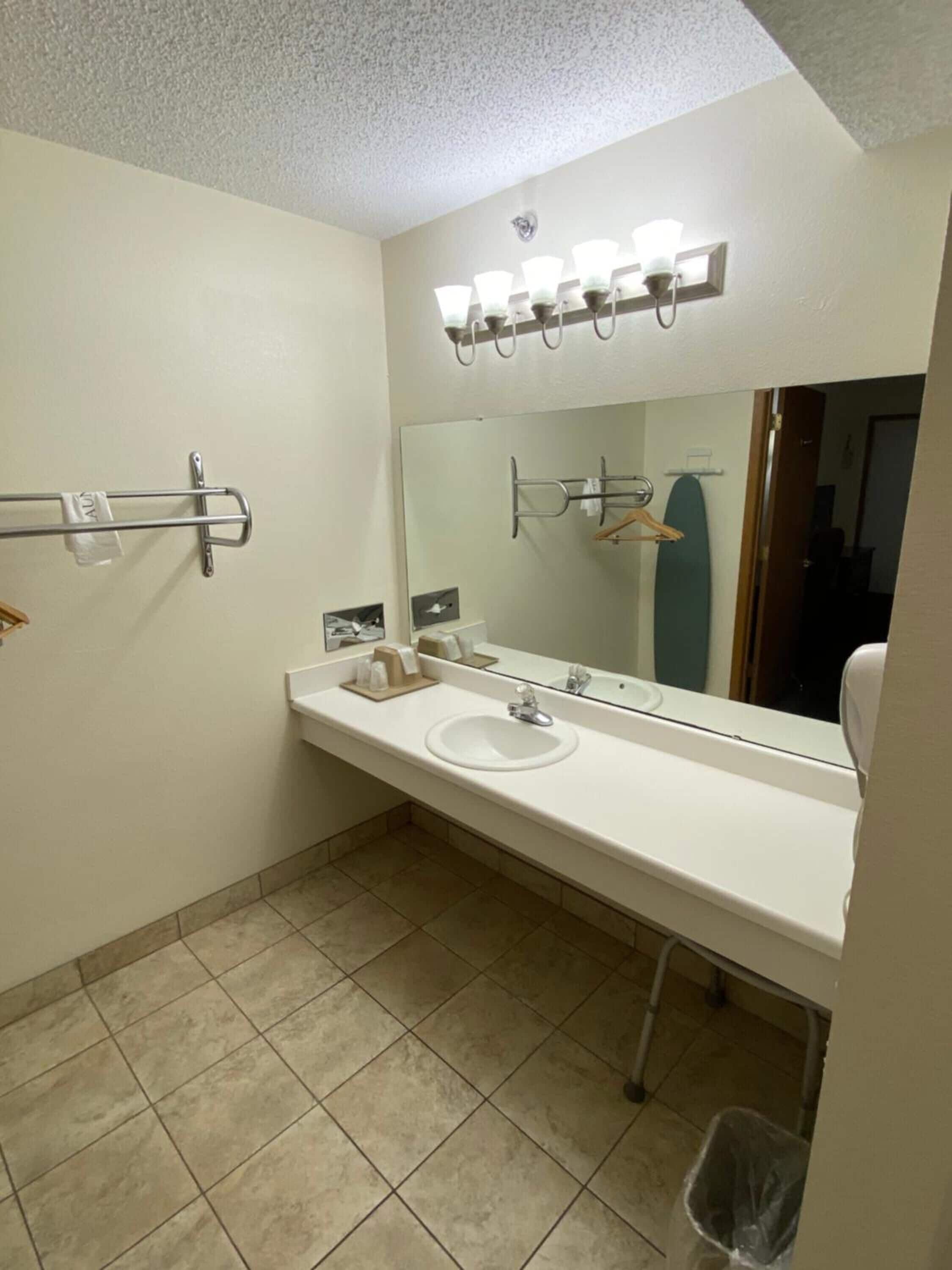A bathroom with a white sink, mirror, towel rack, and a trash bin.