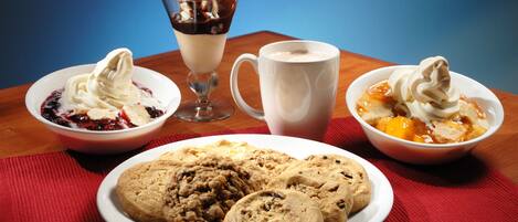 Una mesa de postres con helados en recipientes, una taza y galletas.