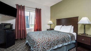 A hotel room with a bed, a TV, a desk, a lamp, and a window with curtains. - Days Inn by Wyndham Fargo/Casselton Waterpark (Casselton)