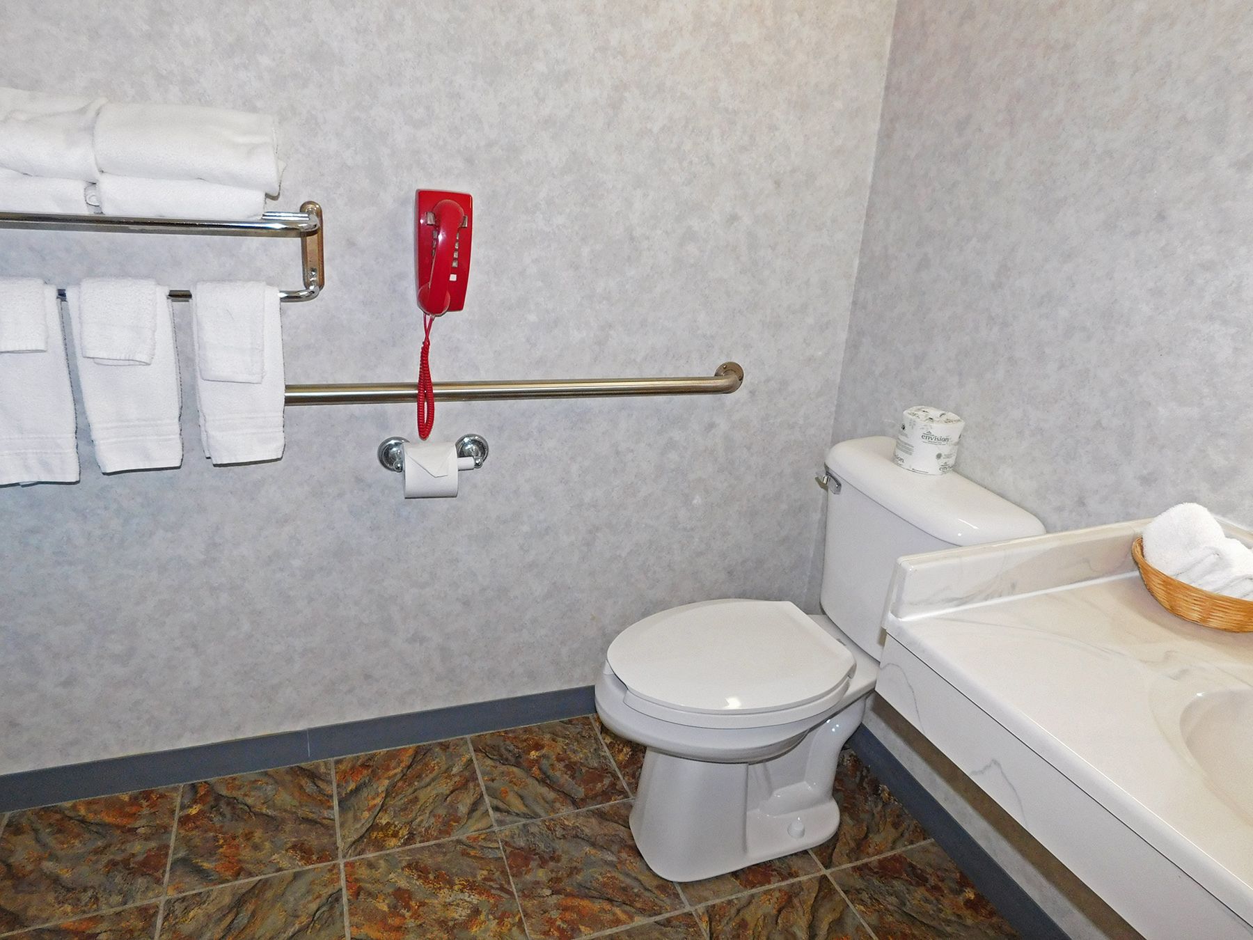 A bathroom with a toilet, a hand dryer, a towel rack with towels, and a basket of towels on the sink.
