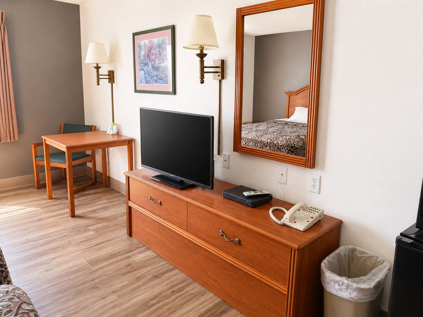 Habitación de hotel con escritorio de madera, televisión, teléfono, espejo y un cuadro en la pared.