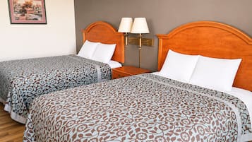 A hotel room with two beds, each with patterned bedding, a nightstand with lamps, and a framed picture on the wall.