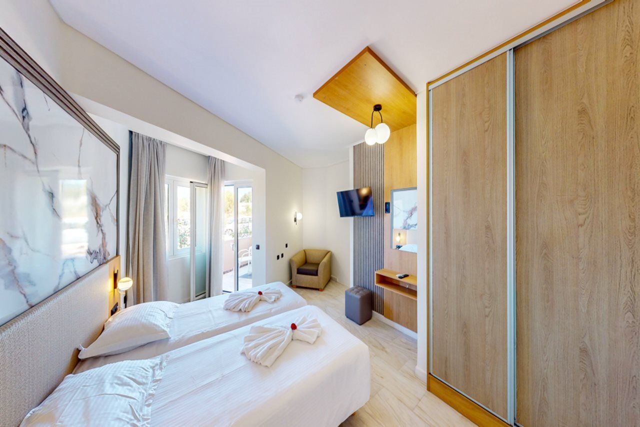 Ett hotellrum med två sängar, en TV, en garderob i trä och ett stort fönster.