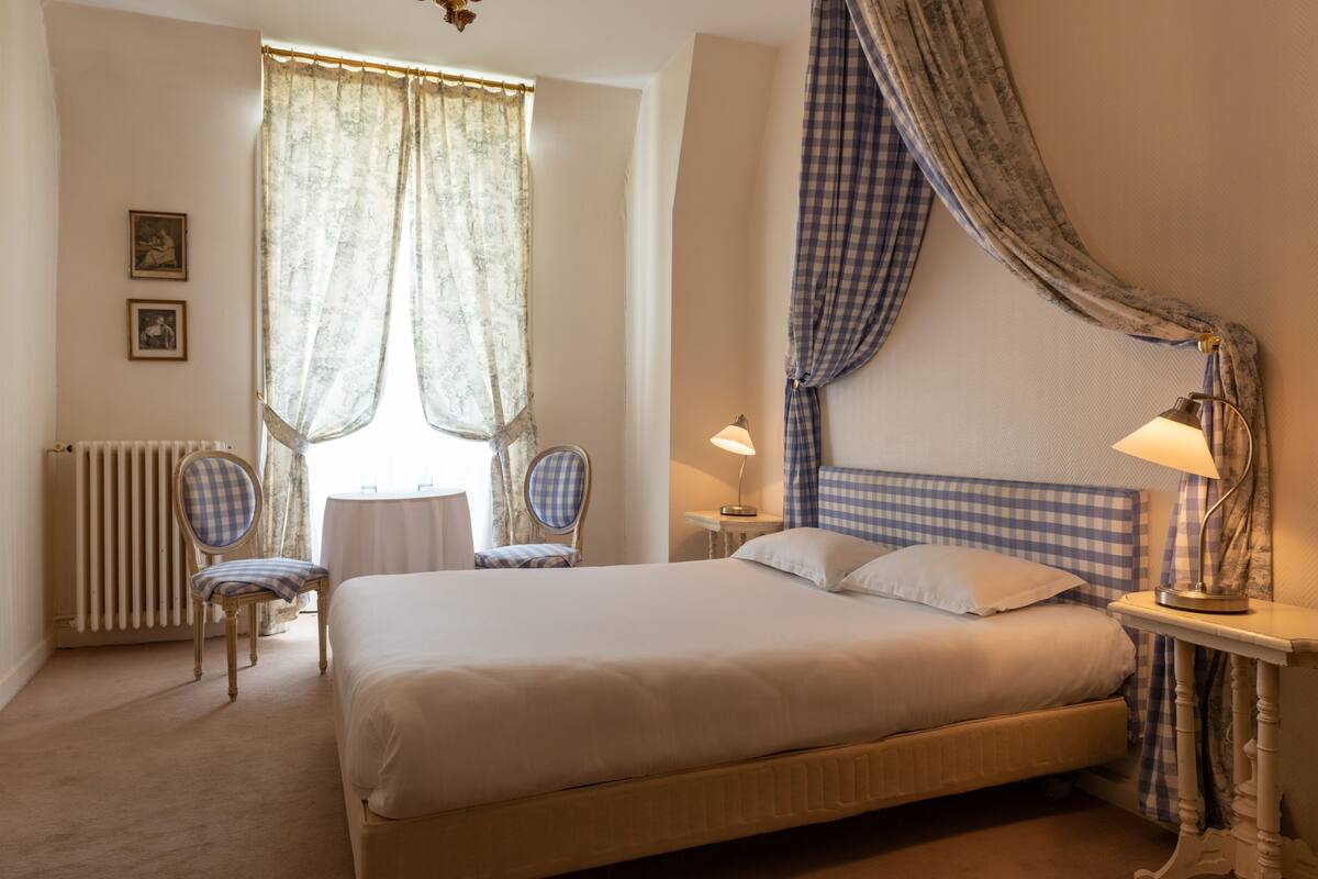 A bedroom with a bed, two chairs, a table, and a lamp.