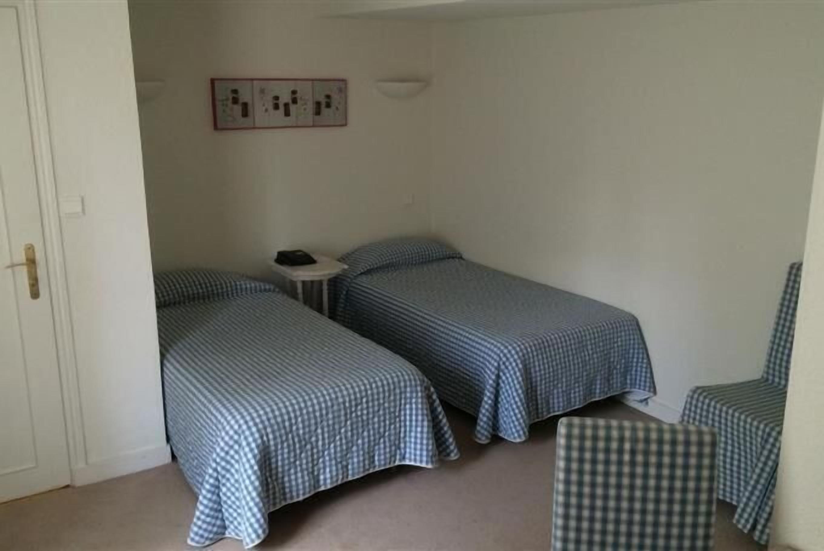 A small, simple room with two single beds, a small table, and a chair.